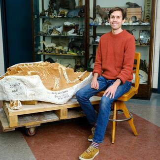 A photograph of Roger Benson, paleontologist, next to a large dinosaur fossil.