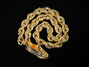 Thick gold chain curled into circular shape with a sneaker-shaped pendant at the end.
