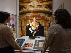 Two visitors stand in front of a Ganesh figure, a Hindu god with an elephant head and human-like body, in a dancing pose.