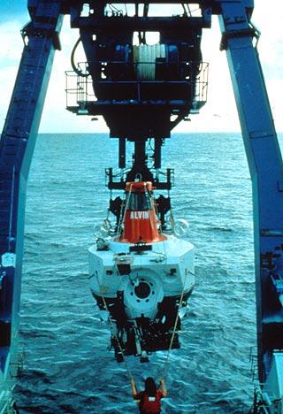 A crane on the stern of a ship holds the deep submergence vehicle ALVIN poised above the sea as it about to be launched.