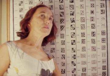 Victoria de la Jara, stands in front of a graphic featuring rows of illustrated Inka tokapu, discrete geometrical motifs in squares.