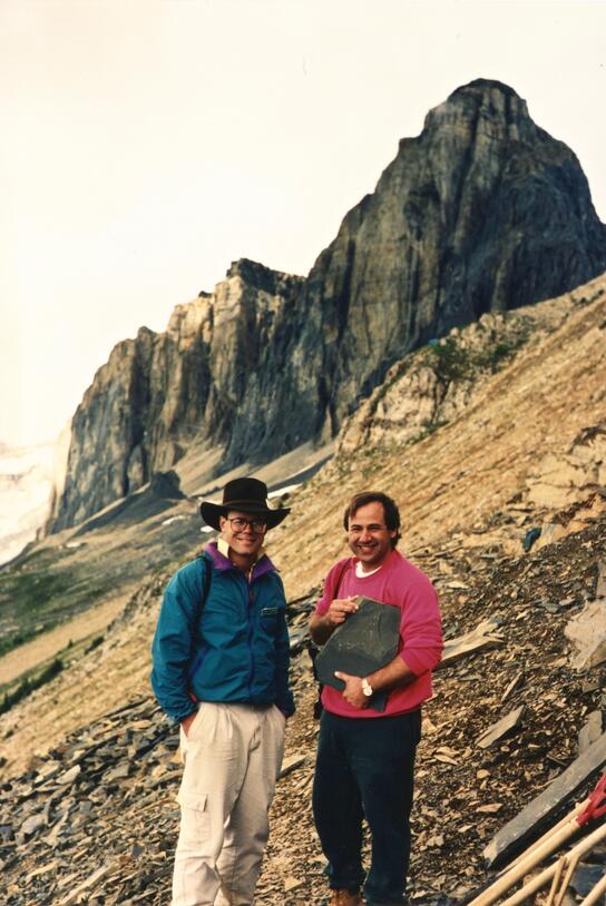 Martin Shugar, holding the fossil of an Anomalocaris claw, stands with another person in front of Mount Wapta.