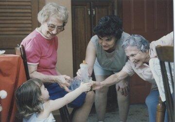 A little girl and three older women clinking glasses in a toast.