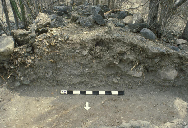 A mound of rocks and dry soil, partly excavated, with a marker on the ground.