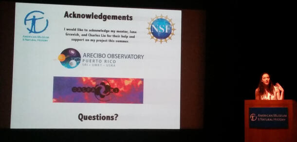Sabrina Berger speaking at a podium on front to the right of a projected slide titled "Acknowledgments," including blurb and 4 company logos.