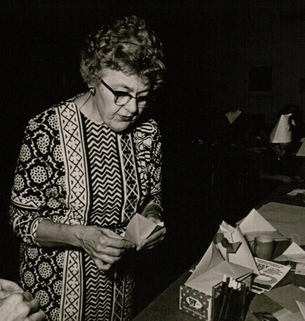 A woman, Alice Gray, standing at a table folding origami.