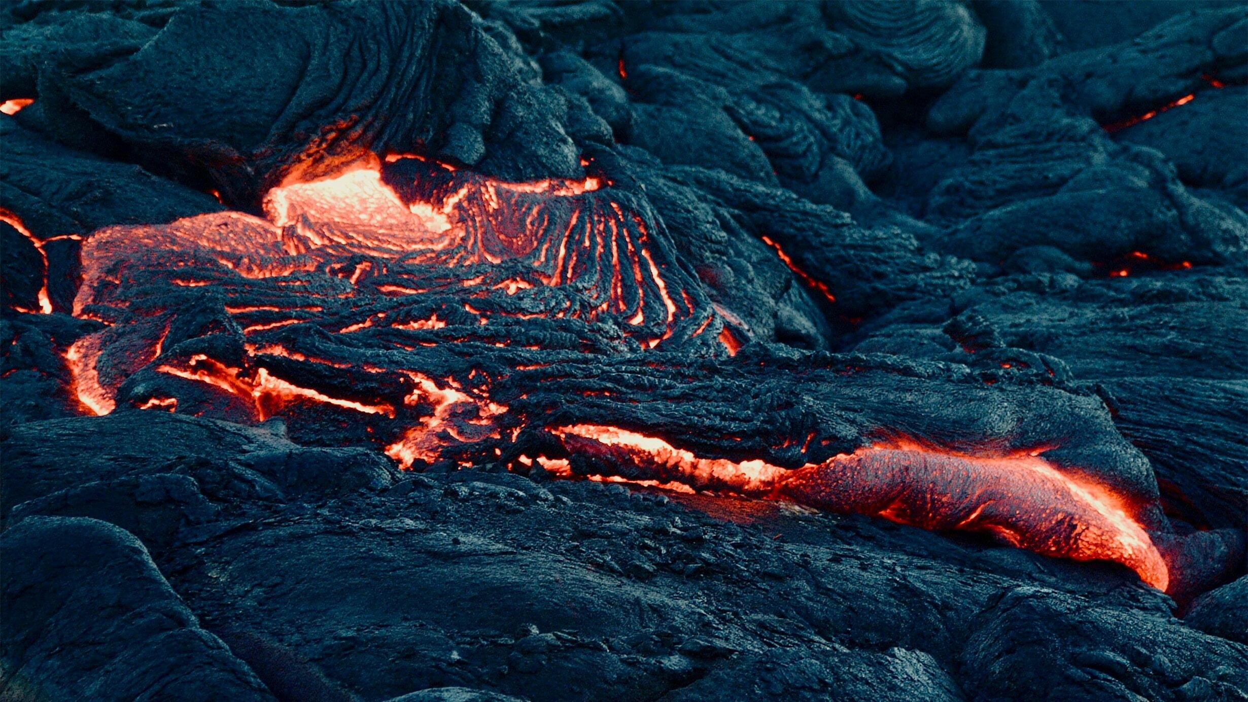 An up-close photo of flowing lava: magma appears as a bright orange, flowing river through cooled black rock.