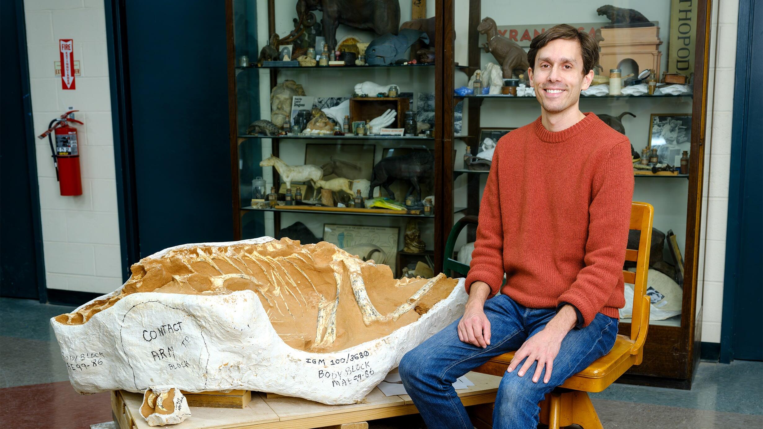 A photograph of Roger Benson, paleontologist, next to a large dinosaur fossil.