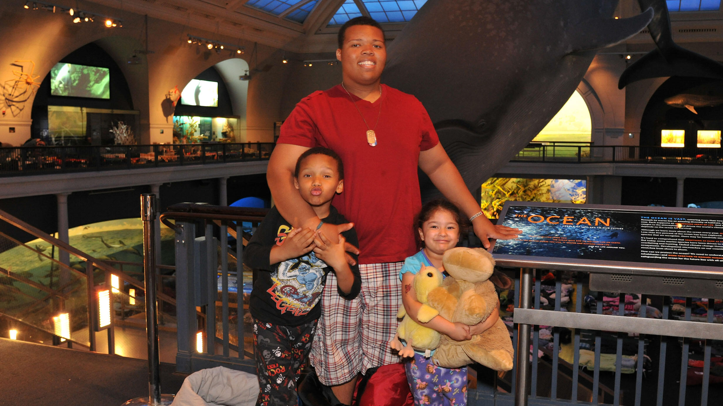 Adult and two children stand in front of the blue whale in the Milstein Hall of Ocean Life.
