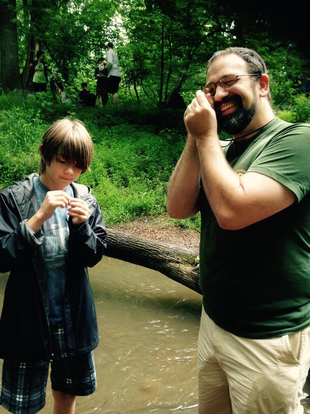Carl Mehling (right) stands beside a child and examines a fossil while standing in a river.