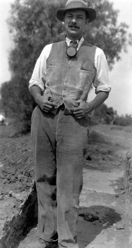 A black and white photo of man, George Vaillant, standing at an excavation site, wearing a fedora hat, waistcoat, and white shirt, with sleeves rolled up.