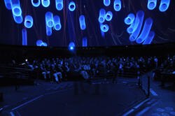 audience in Hayden Planetarium watching blue cylinder-like images overhead