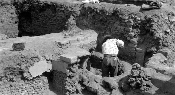 A person standing and working in a excavation area composed of partially exposed low brick walls. The photo caption states: "Sunken patio looking north."
