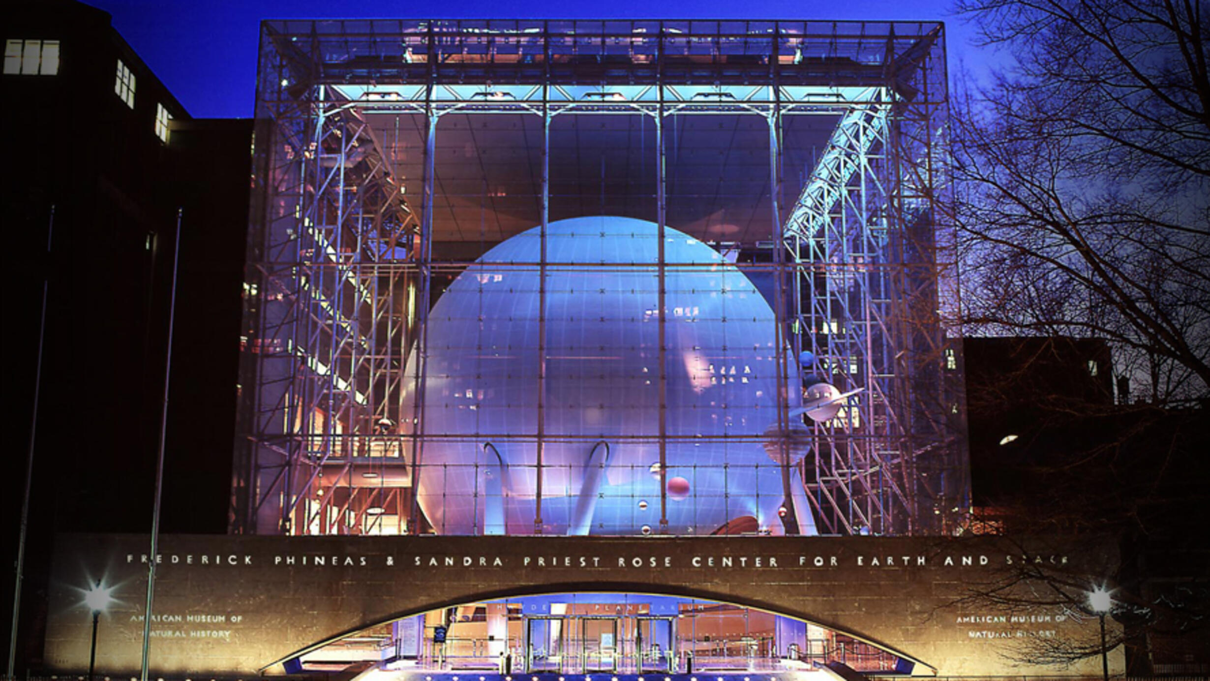 The Hayden Sphere inside the cubical Rose Center pictured from outside the entrance, illuminated at nighttime.