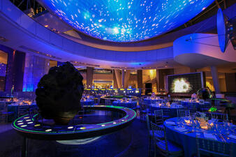 Cullman Hall of the Universe with dramatic lighting and tables set in preparation for a wedding or social celebration.