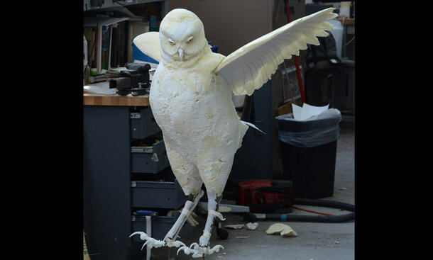 Partially completed owl model stands on the floor in the exhibit construction area.