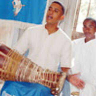 Three santería practitioners playing a drum and singing.