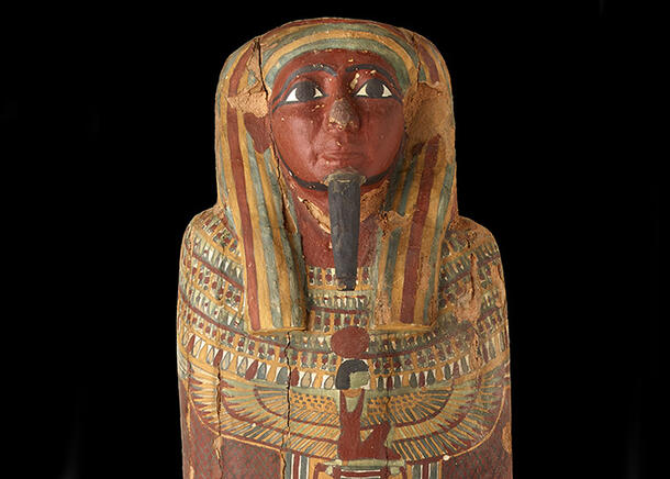 Detail of the head of the coffin shows a painted face with a long slim beard, wearing a headdress, with illustrated figures decorating the body.