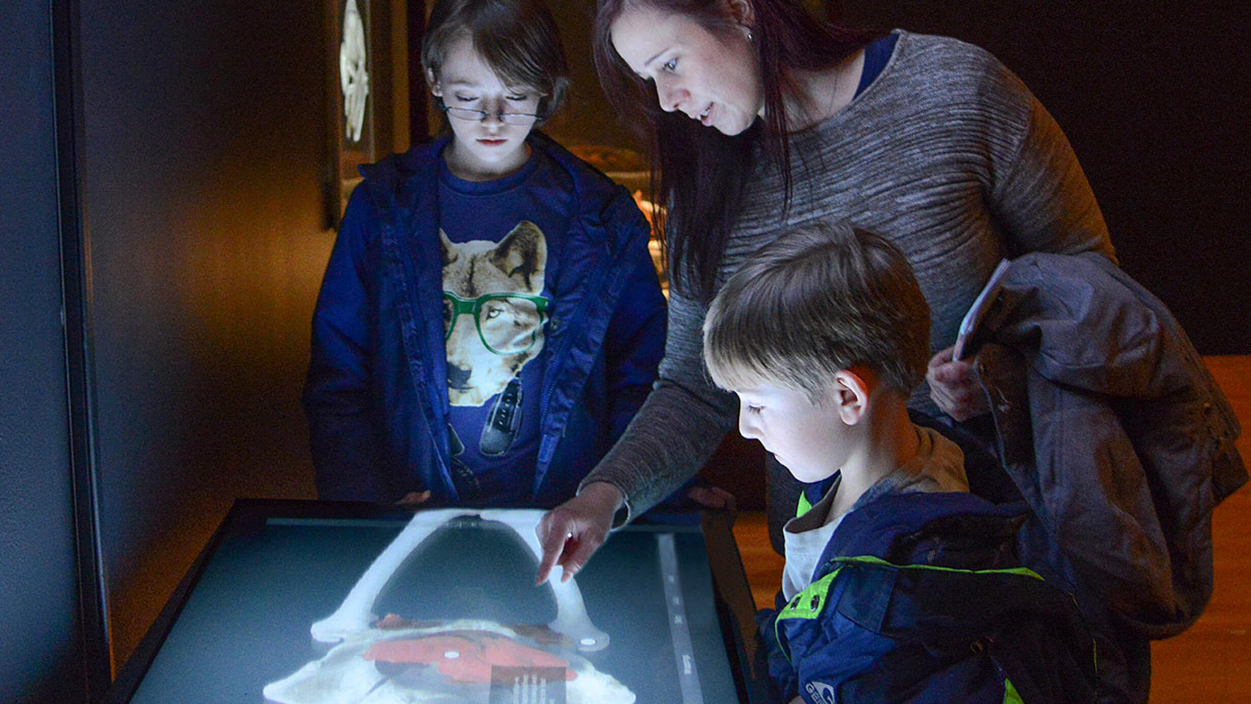 Two children and an adult gather around a tabletop digital touch screen that allows them to see "inside" the mummy via CT scans.
