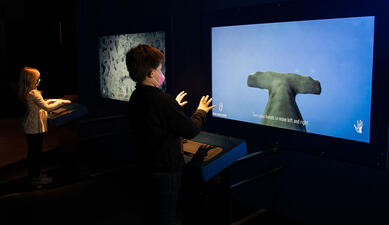 Two children gesture at side-by-side interactive screens.