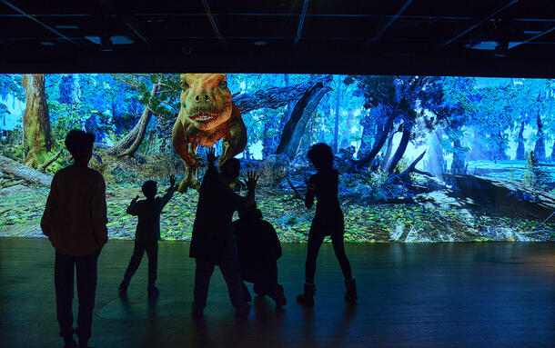 Silhouetted visitors watch the giant wall screen animation in the T. rex: Ultimate Predator exhibition.