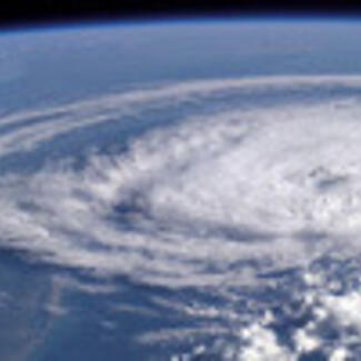A huge spiral white cloud mass against the blue surface of earth viewed from space.
