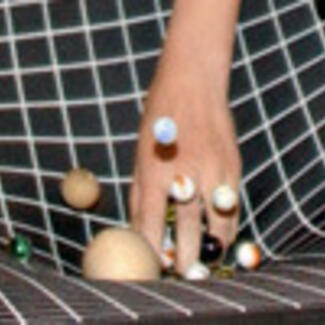 A photo captured at the moment a human hand strikes a net-like surface causing small spherical objects to bounce up.