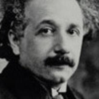 A closeup photo of the head and shoulders of a man with a mustache and wavy hair, Albert Einstein.
