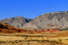 A picture of a rolling plain with  red rock, dry vegetation, and rocky hills in the background