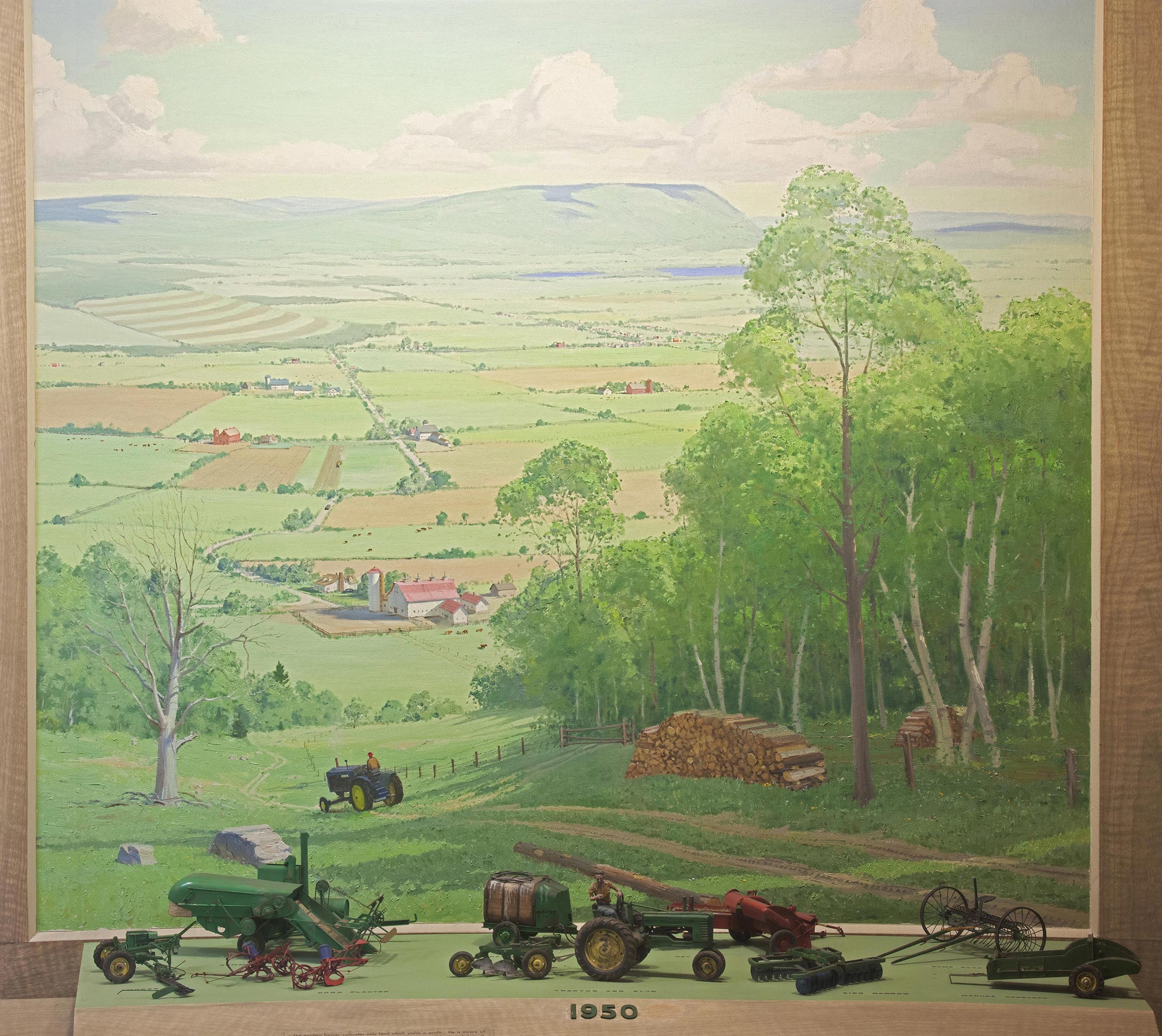 Scale models of farming tools from 1950 with background painting of a landscape with a farm.