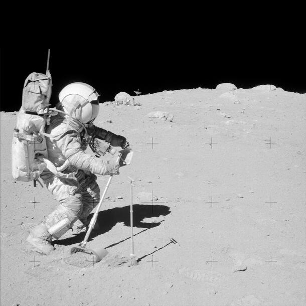 An astrounat walking on the Moon wearing a space suit uses instruments similar to a broom and a handled dustpan to collect samples.