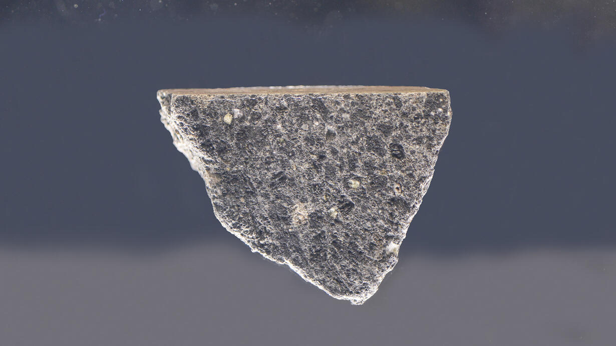 A light gray triangular rock called kreep basalt suspended in glass.