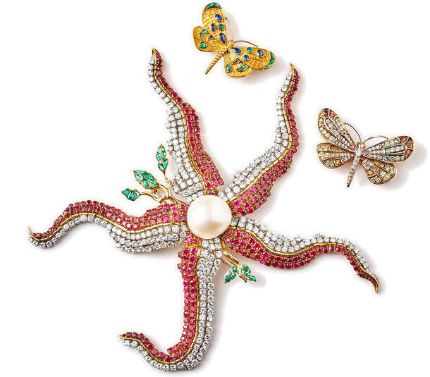 Jeweled brooch in the shape of a starfish next to two jeweled pins in the shape of butterflies.