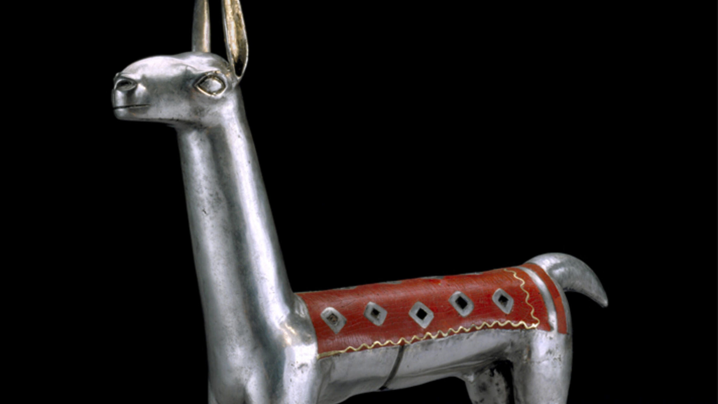 A small silver-colored figurine of a llama with a long neck and erect ears, with a narrow rectangular red-and-gold blanket along the length of its back.