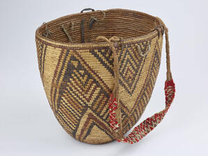 Round woven basket with triangular patterned details and a woven handle with brightly colored detailing. 