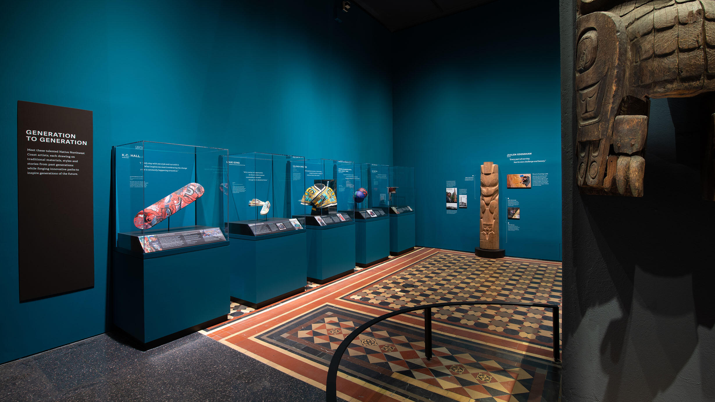 The Generation to Generation gallery within the Northwest Coast Hall contains a cedar pole carving and glass display cases containing works of art.