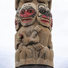 Four wooden carved figures in circular formation with differing painted designs on each face.