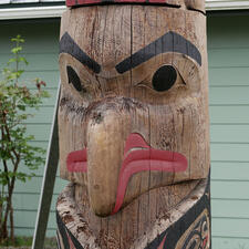 Carved wooden figure with long, downturned beak, bright colored mouth and black eyes and eyebrow.