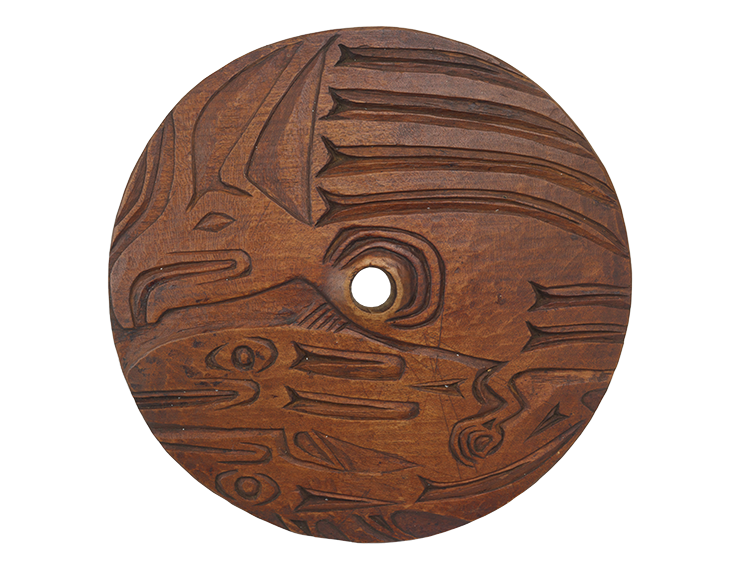 Carved wooden circle with hole in the middle with stylized designs depicting a bird and fish.