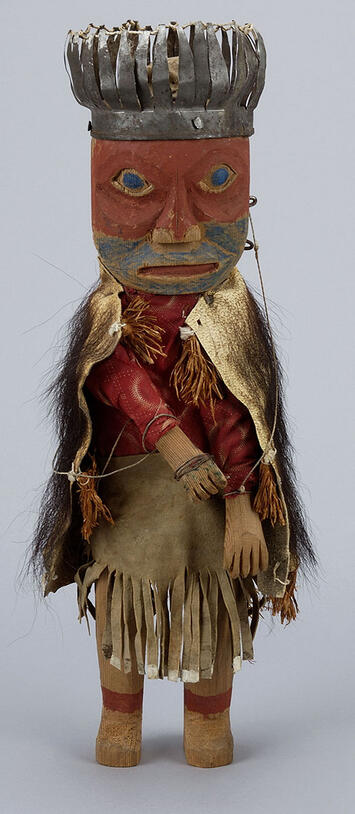 Carved figurine of a person with a painted face, wearing a crown, and dressed in a hide robe hair and skirt.