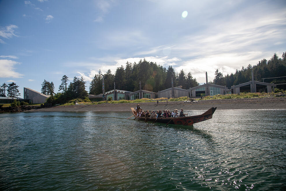A group of people paddle a large wooden canoe near a shoreline.