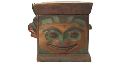 The side of a wooden carved chest with a face carved into it, painted in bright colors.