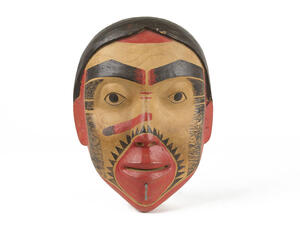 Carved, painted wooden mask of woman's face with brightly painted face and designs around the mouth and cheeks.