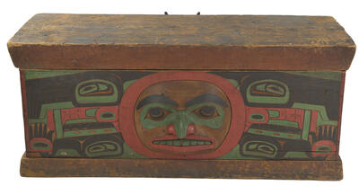 Wooden chest with carved face at center and additional painted designs surrounding the face, painted in multiple colors. 