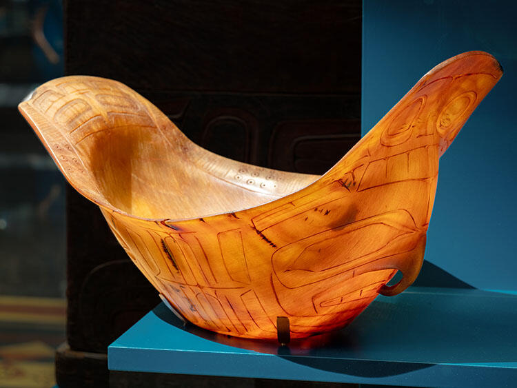 Translucent amber colored bowl curved on both sides with delicate carved figure on the side in a museum display case.