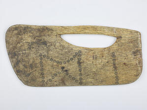 Carved cedar in a rectangular, blade like shape, with a carved out space that acts as a handle.