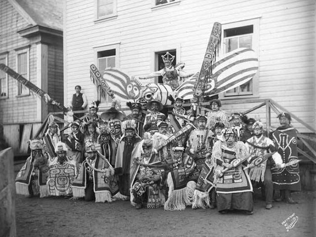 Archival black and white group portrait of about twenty people dressed in ceremonial regalia. 