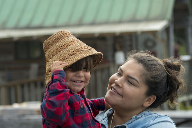 Woman holds a child that is wearing a woven hat.