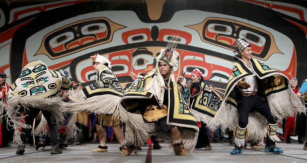 Three dancers wear heavily fringed ceremonial robes.