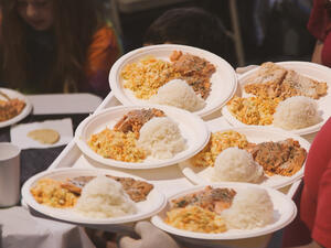 Unseen person holds a tray of 6 paper plates full of food, each with rice, salmon and vegetables.